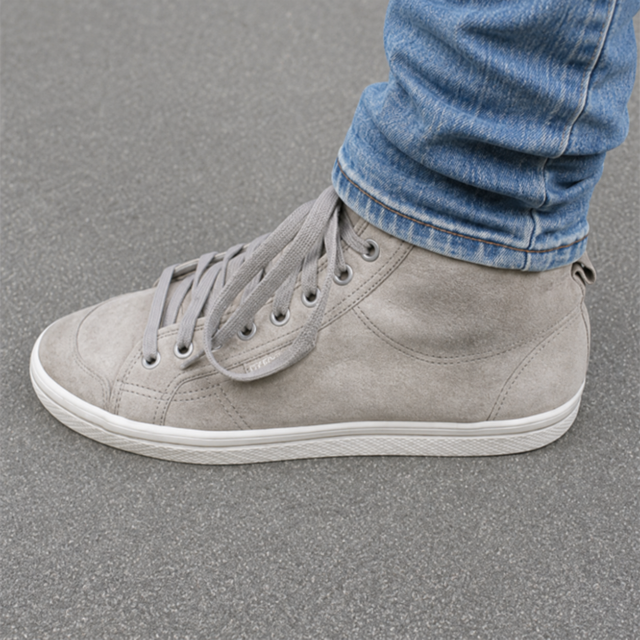 Grauer Sneaker mit Jeanshose auf Asphalt